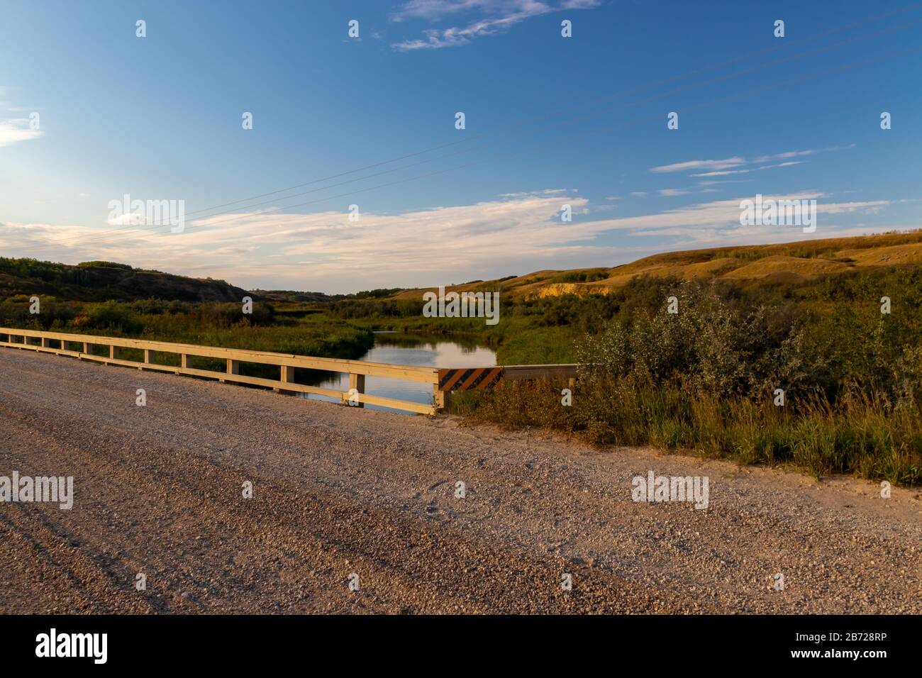 Una vista di un ponte isolato su un flusso tranquillo che attraversa una valle nelle ampie praterie aperte di Saskatchewan, Canada Foto Stock