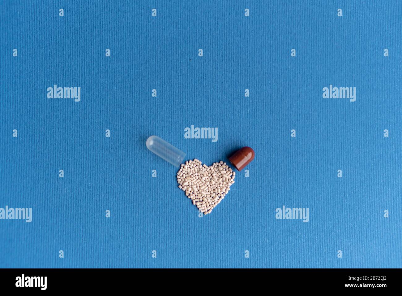 Granuli versati da una capsula a forma di cuore su un classico sfondo blu. Medicinali a forma di cuore. Simbolo del cuore disegnato dalle pillole. Foto Stock