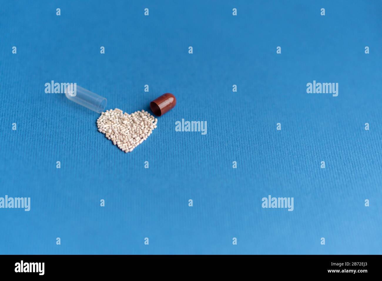 Granuli versati da una capsula a forma di cuore su un classico sfondo blu. Medicinali a forma di cuore. Simbolo del cuore disegnato dalle pillole. Foto Stock