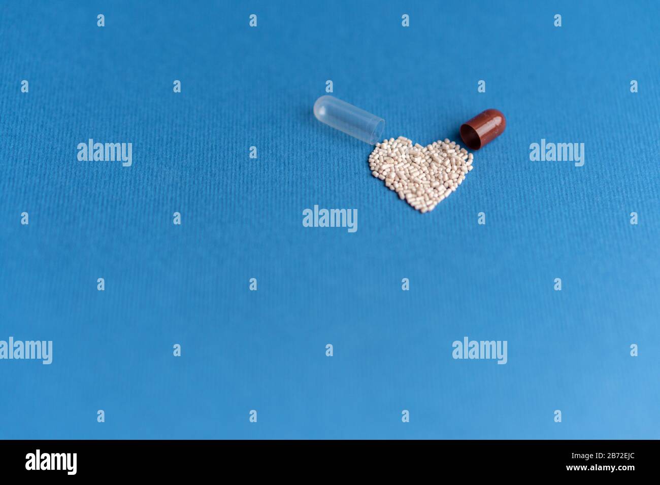 Granuli versati da una capsula a forma di cuore su un classico sfondo blu. Medicinali a forma di cuore. Simbolo del cuore disegnato dalle pillole. Foto Stock