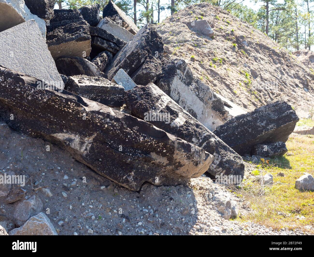 Montagna di strada demolizioni pavimentazione, asfalto e calcestruzzo macerie, sabbia, ghiaia, aggregati in primo piano, enorme pile di sabbia sfondo, pini Foto Stock