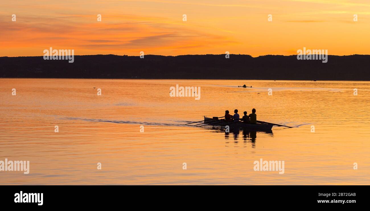 Silhoutte di una squadra di quattro in una barca a remi su un lago. Dopo il tramonto. In lontananza una seconda barca a remi. Concetto di lavoro di squadra, competizione, vittoria Foto Stock