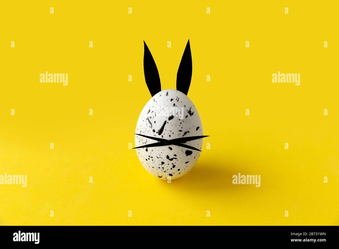 Uovo di Pasqua con orecchie bunny e faccia su sfondo giallo Foto Stock
