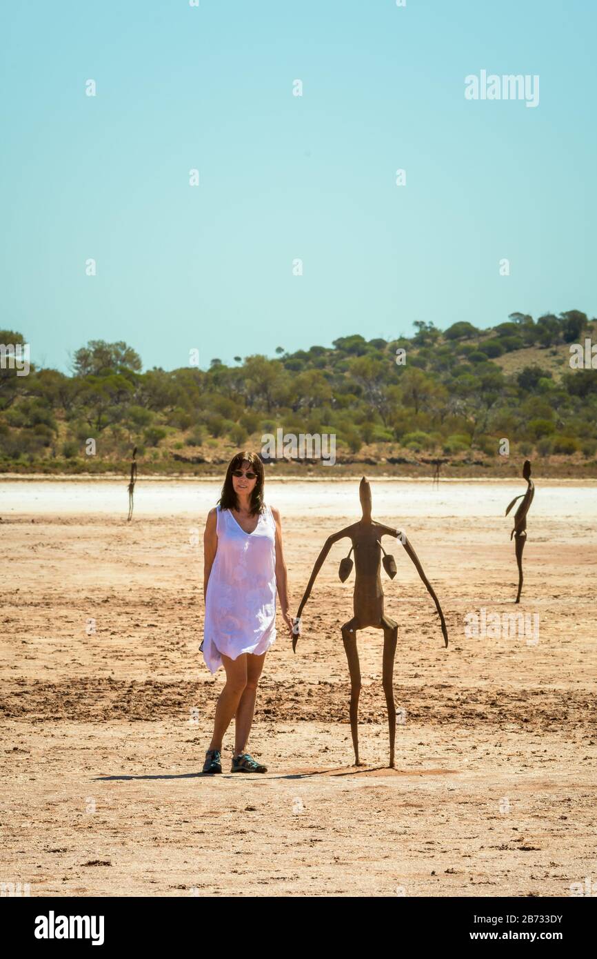 Fornendo scala, una turista femminile in abito bianco si trova accanto a una delle sculture in metallo dell'artista britannico Antony Gormley sul lago Ballard. Foto Stock