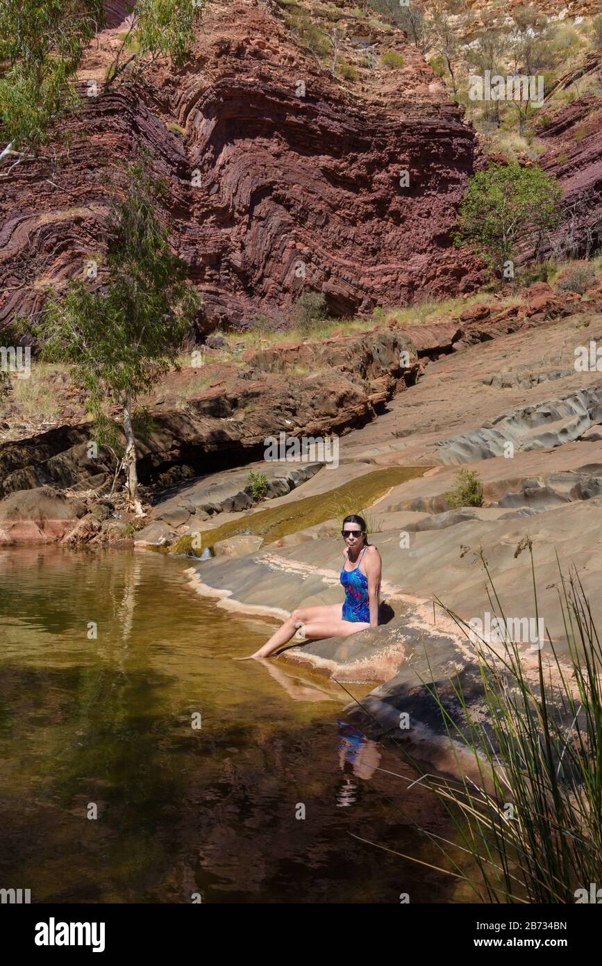 Vista delle donne turistiche in un costume da bagno blu brillante che si trova accanto ad una cristallina acqua dolce della frastagliata gola di Hamersley nell'Australia Occidentale. Foto Stock