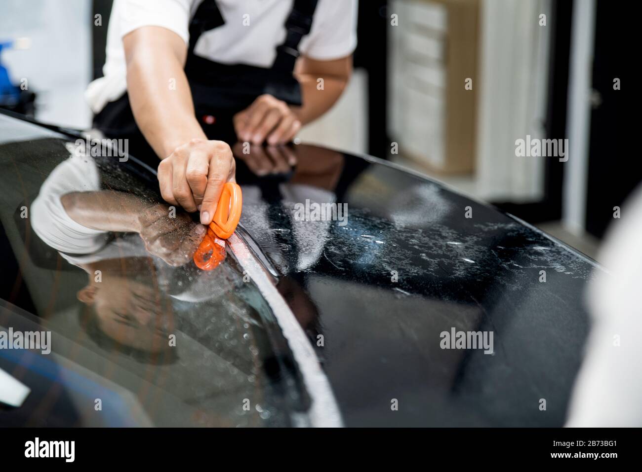 Primo piano di un'auto che si specializzano raddrizzando le mani avvolgente pellicola trasparente per la protezione con un tagliafilm per tagliare una pellicola. Installazione PPF. Foto Stock