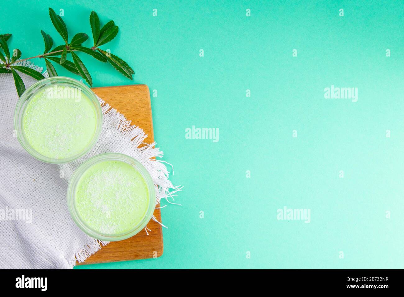 Yogurt di limone alla menta con kiwi in ciotole per insalata su una tavola di legno con rami verdi su uno sfondo rosa Foto Stock