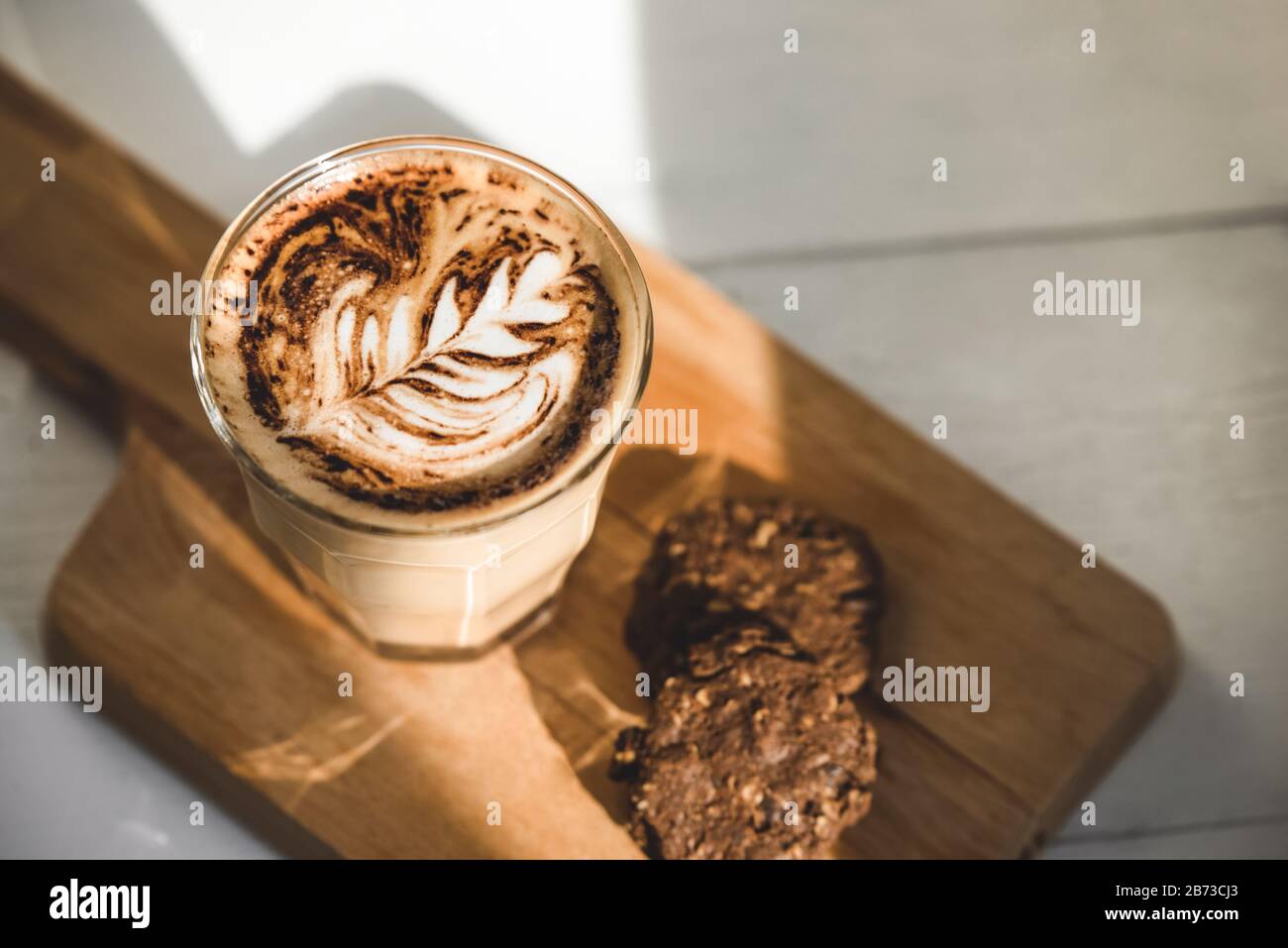 Caffè caldo in lattina in bicchiere con biscotti al cioccolato su un piatto di legno in caffetteria per la colazione Foto Stock