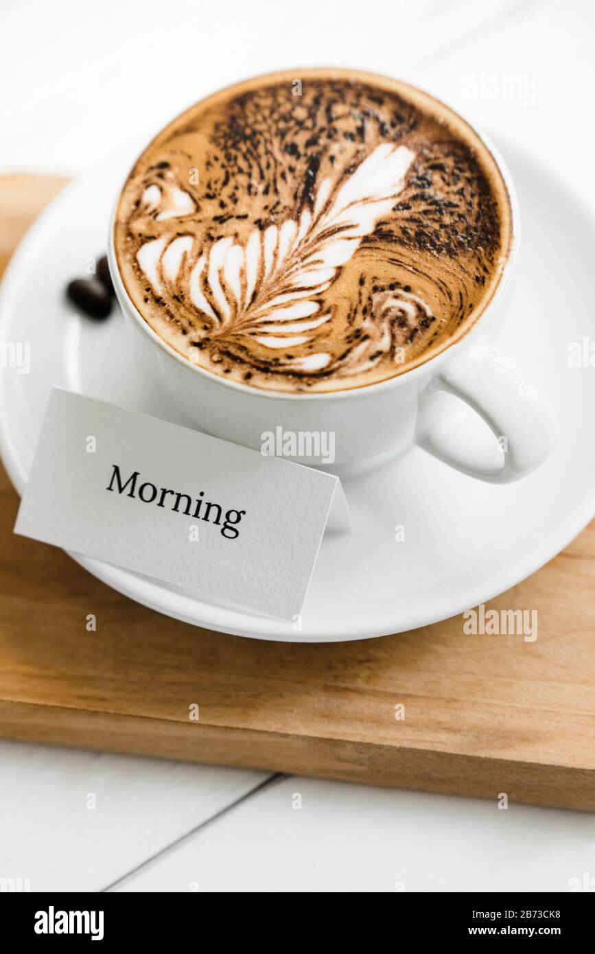 Fern pattern latte art caffè in tazza accanto testo di saluto su vassoio di legno in caffè Foto Stock
