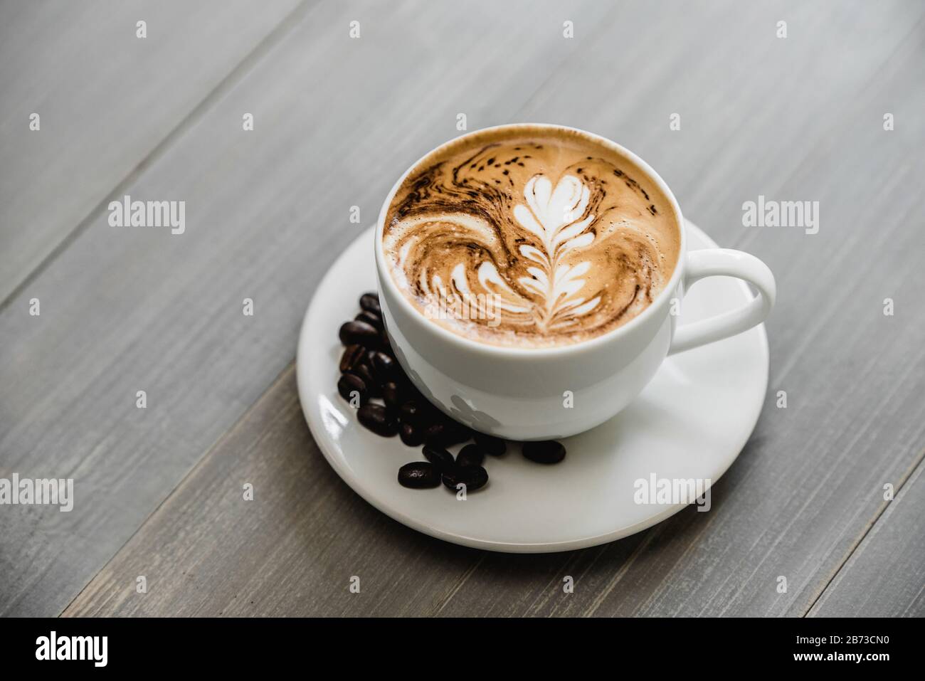 Caffè appena preparato con latte art in fern pattern in tazza bianca su tavolato in legno Foto Stock
