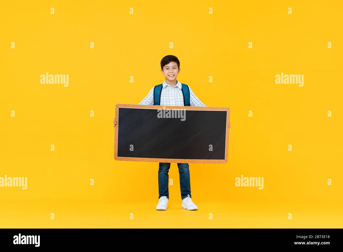 Sorridente bel 10 anni di razza mista ragazzo tenendo nero vuoto isolato su sfondo giallo studio per il concetto di istruzione Foto Stock