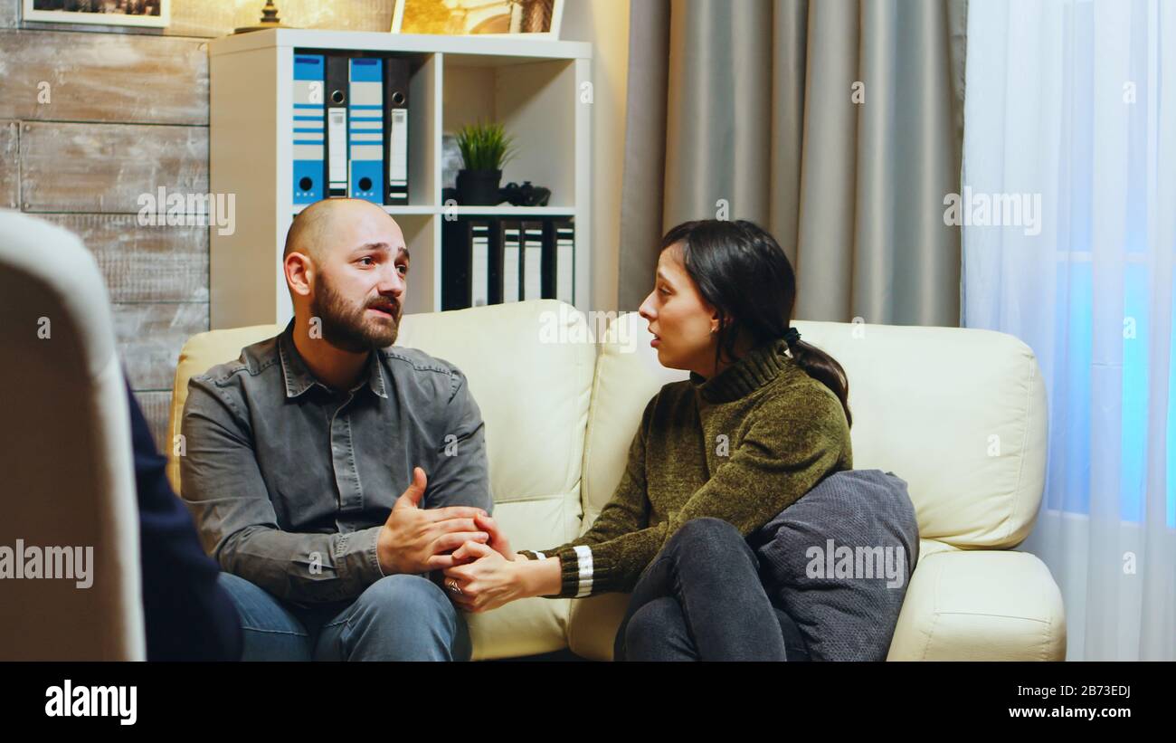 Triste ragazza che tiene le mani del marito seduto sul divano a terapia di coppia. Terapista che dà la guida alla coppia stressata. Foto Stock