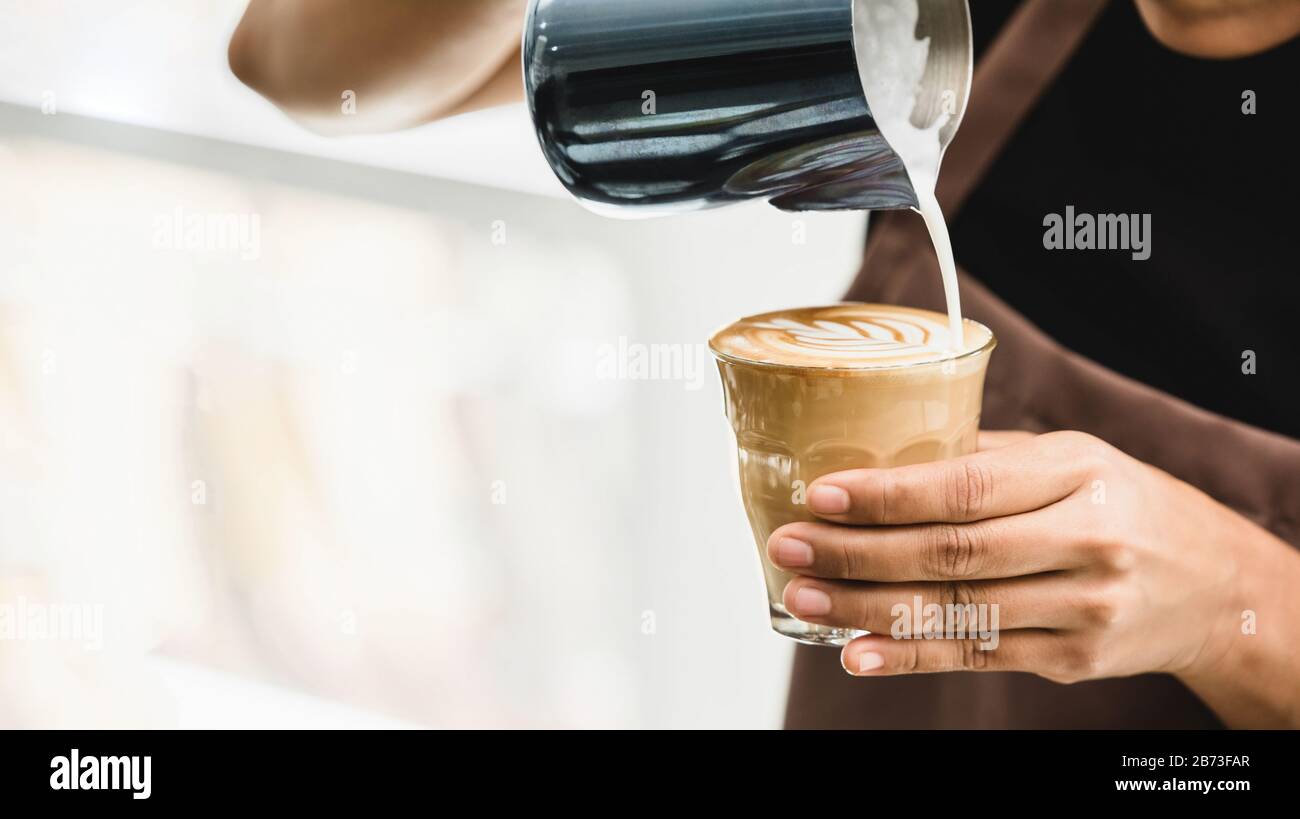 Barista professionista che versa il latte cotto a vapore in una tazza di vetro del caffè facendo bella arte latte Rosetta modello in caffè Foto Stock