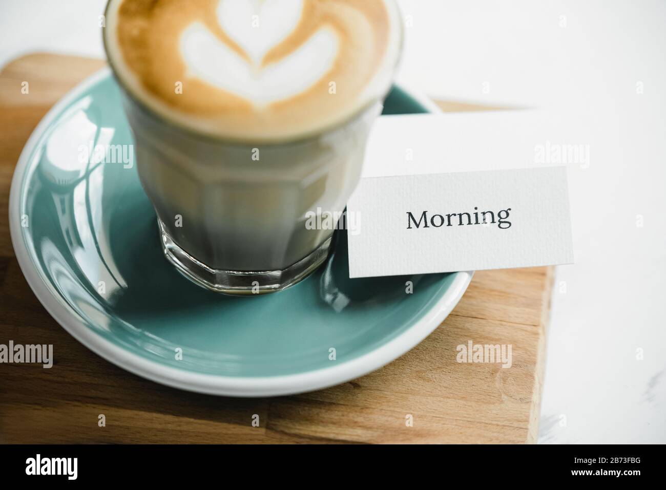 Carta da tavola con testo mattutino e caffè cappuccino appena preparato con splendida arte in latte su tavola di legno pronto a bere Foto Stock