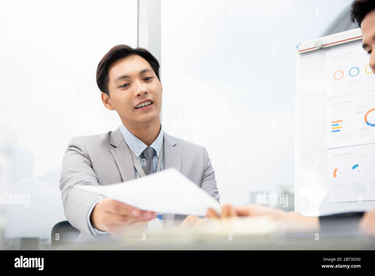 Allegro uomo d'affari asiatico che suggerisce il documento di business plan al cliente alla riunione in ufficio Foto Stock