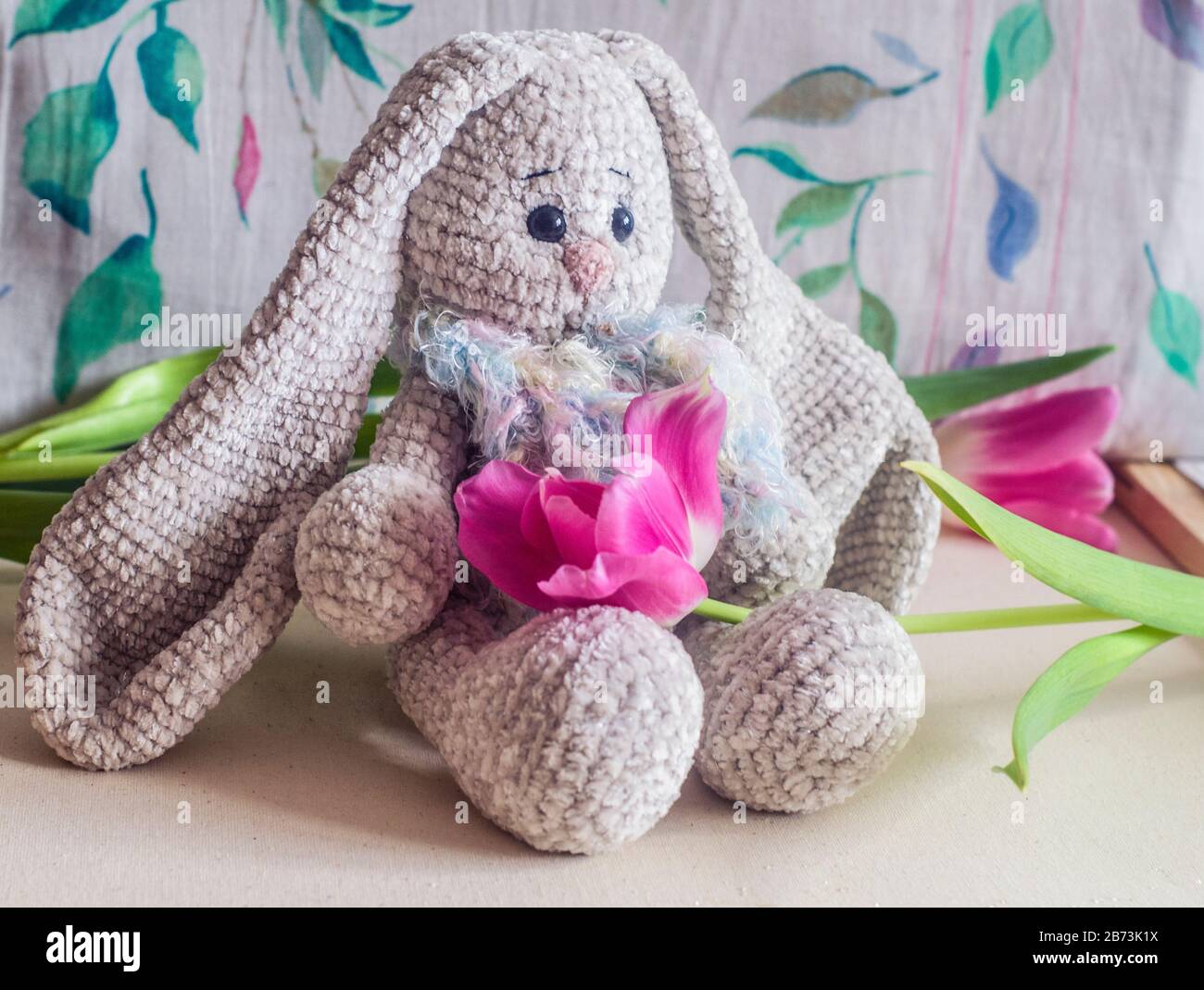 Coniglio lavorato a mano grigio chiaro con tulipani rosa . Giocattolo per bambini. Modello a crochet. Produzione artigianale. Foto Stock