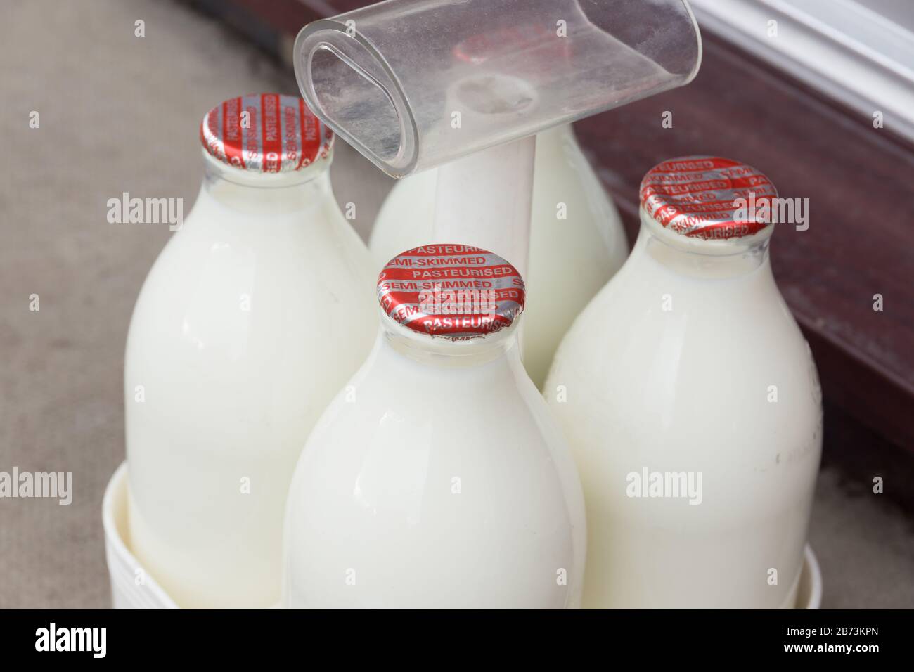 Latte fresco parzialmente scremato in bottiglie di vetro riciclabili consegnate alla porta da un lattiere tradizionale Foto Stock