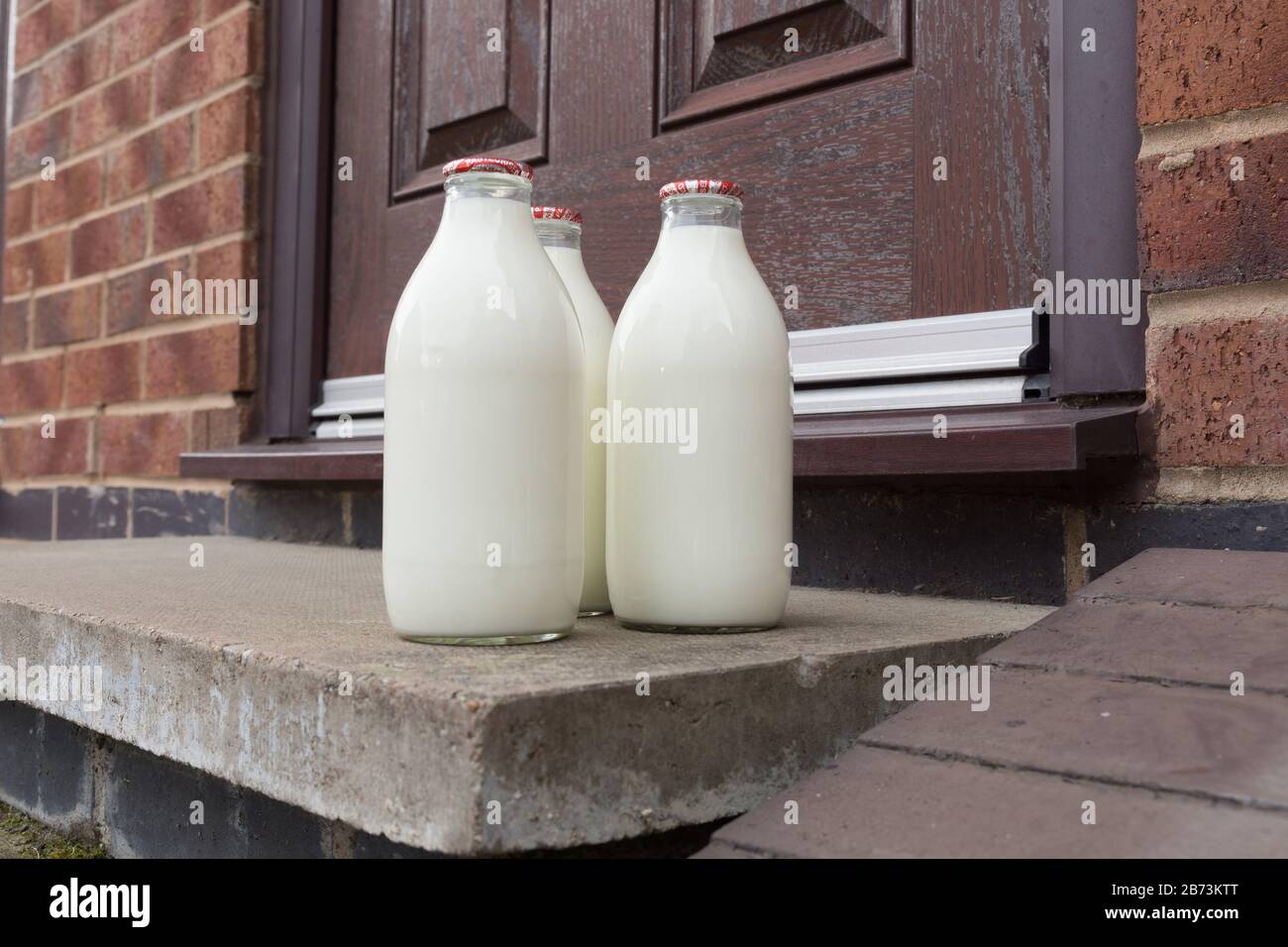 Latte fresco in biberon di vetro riciclabile consegnato alla porta da un tradizionale lattiere Foto Stock