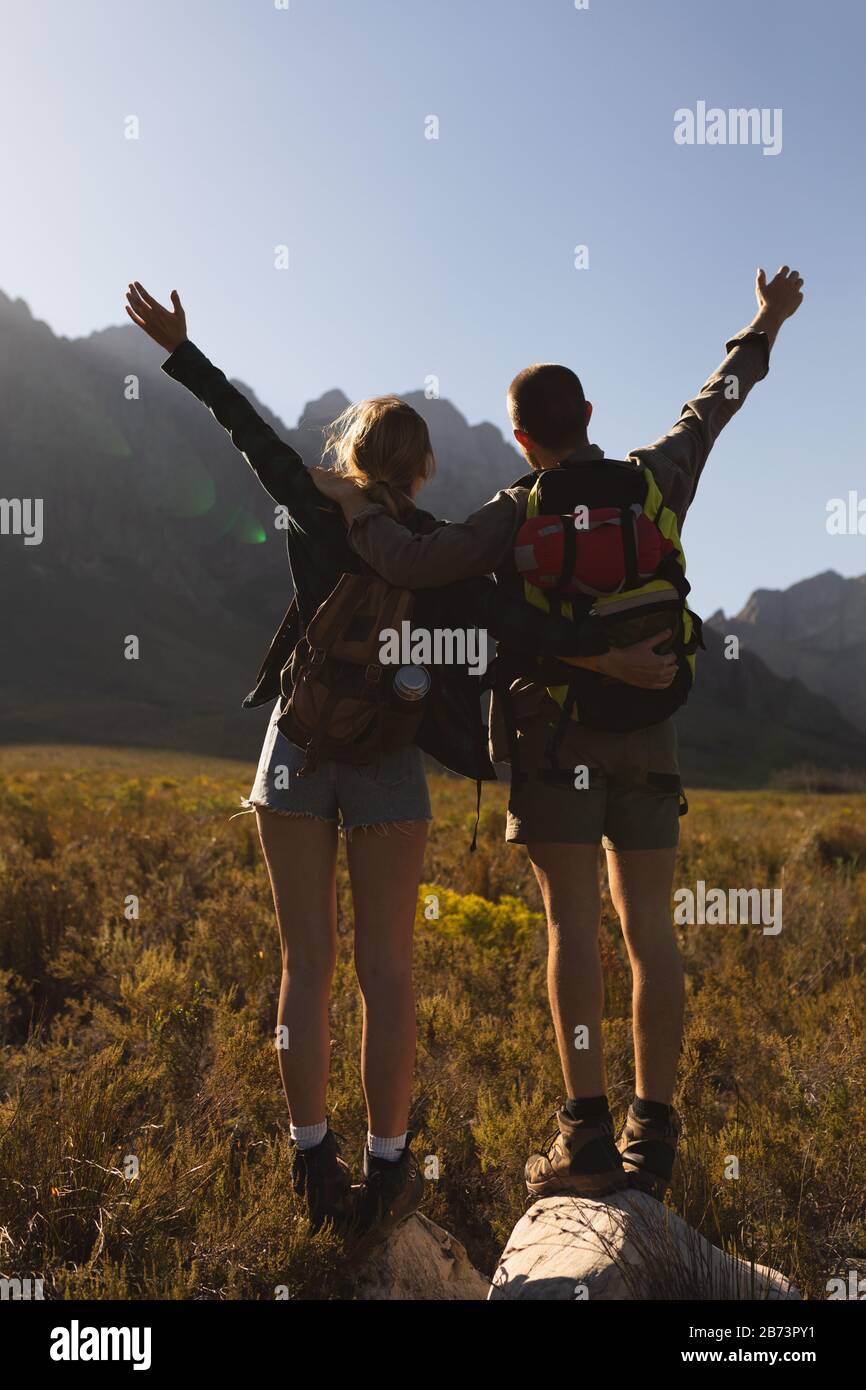 Vista posteriore della coppia con zaini che alzano le braccia in aria Foto Stock