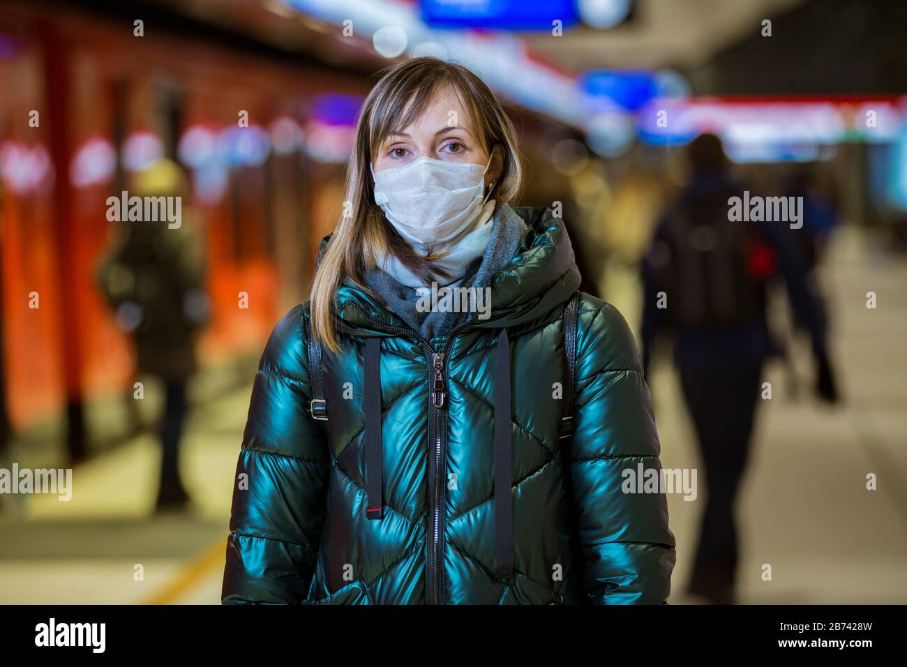 Donna in giacca d'inverno con maschera protettiva sul viso in piedi sulla stazione della metropolitana, in attesa di treno, guardando preoccupato. Misure preventive Foto Stock