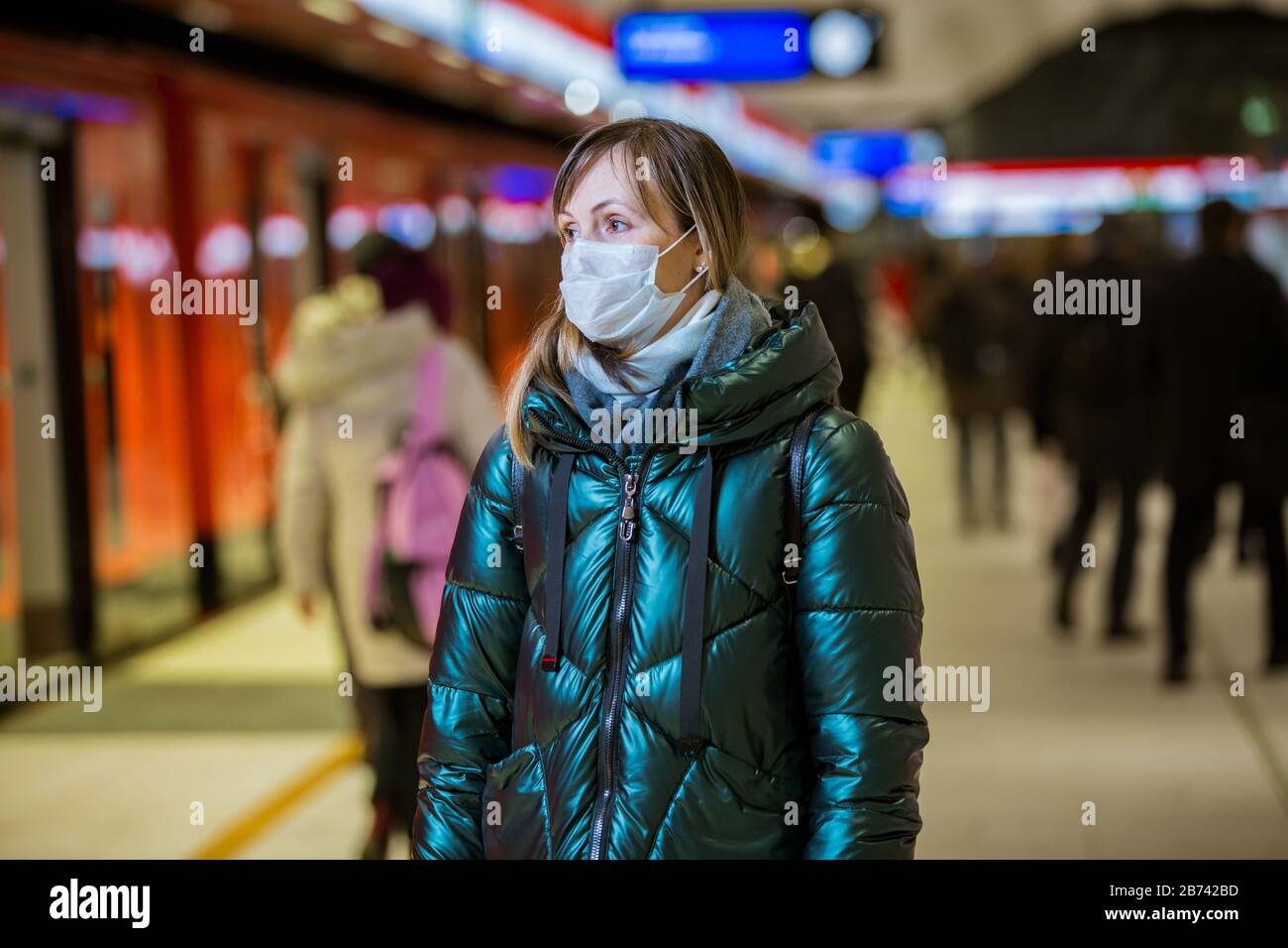 Donna in giacca d'inverno con maschera protettiva sul viso in piedi sulla stazione della metropolitana, in attesa di treno, guardando preoccupato. Misure preventive Foto Stock