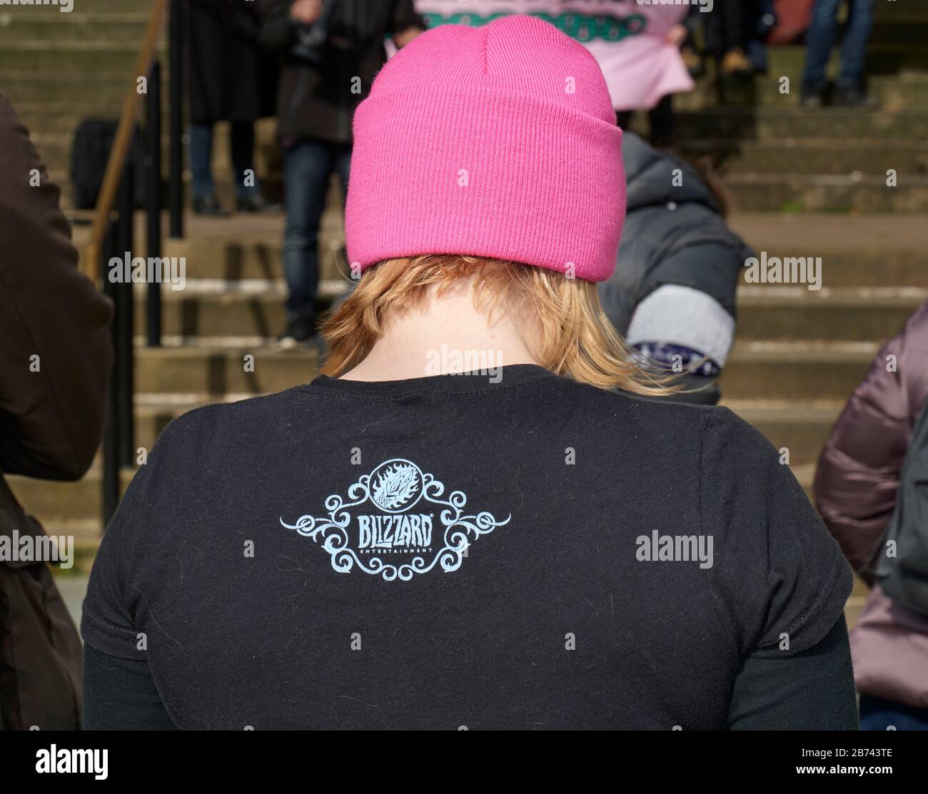 Retro di giovane donna con capelli biondi con cappello rosa e camicia nera. Foto Stock