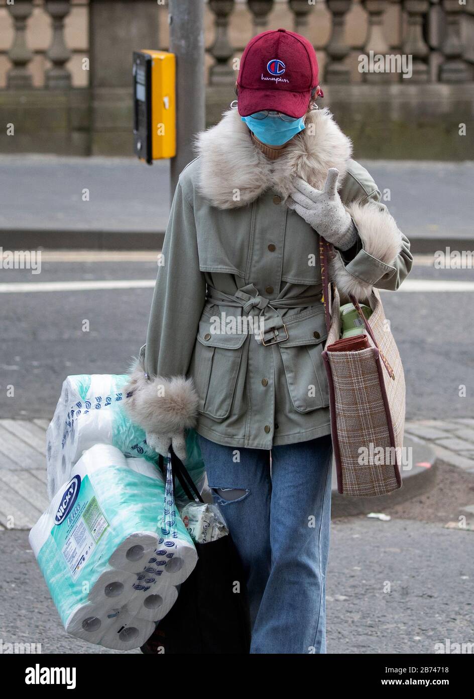 Una donna che indossa una maschera facciale protettiva e che trasporta i rifornimenti di rotoli di carta igienica attraversa la strada sul Royal Mile, Edimburgo, mentre il più alto scienziato del governo ha riscaldato che fino a 10,000 persone nel Regno Unito sono già infettate. Foto Stock
