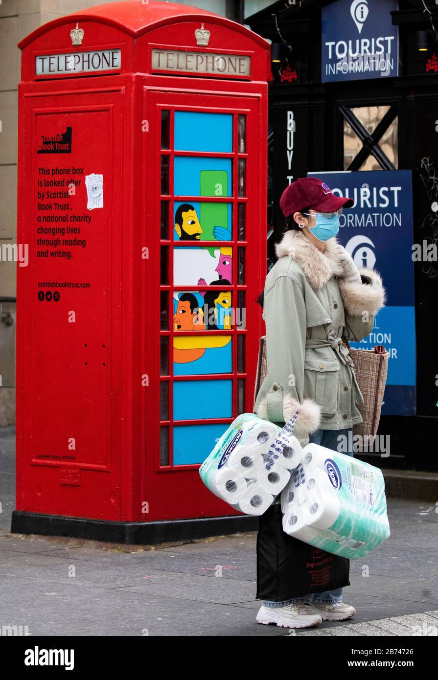 Una donna che indossa una maschera facciale protettiva e che trasporta i rifornimenti di rotoli di carta igienica attraversa la strada sul Royal Mile, Edimburgo, mentre il più alto scienziato del governo ha riscaldato che fino a 10,000 persone nel Regno Unito sono già infettate. Foto Stock