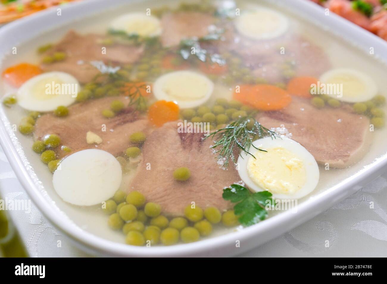 Carne gelata con lingua di manzo, piselli, carote, erbe aromatiche. Un piatto sul tavolo per una festa. Antipasto freddo. Foto Stock