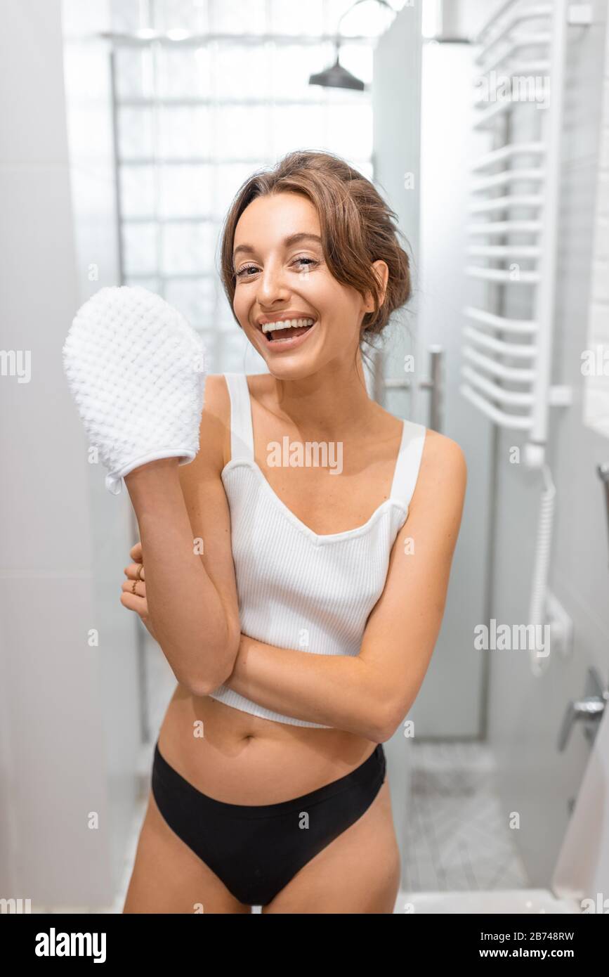 Ritratto di una giovane e allegra donna con un guanto doccia in bagno. Concetto di self care e wellness Foto Stock