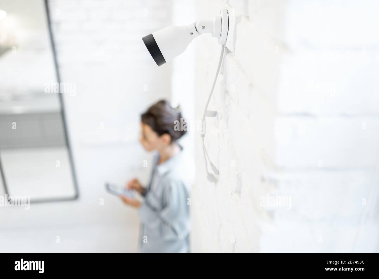 Woman controlla la videosorveglianza domestica con uno smartphone all'interno, la vista dall'alto e la telecamera ip in primo piano. Concetto di sistemi di sicurezza domestica wireless Foto Stock