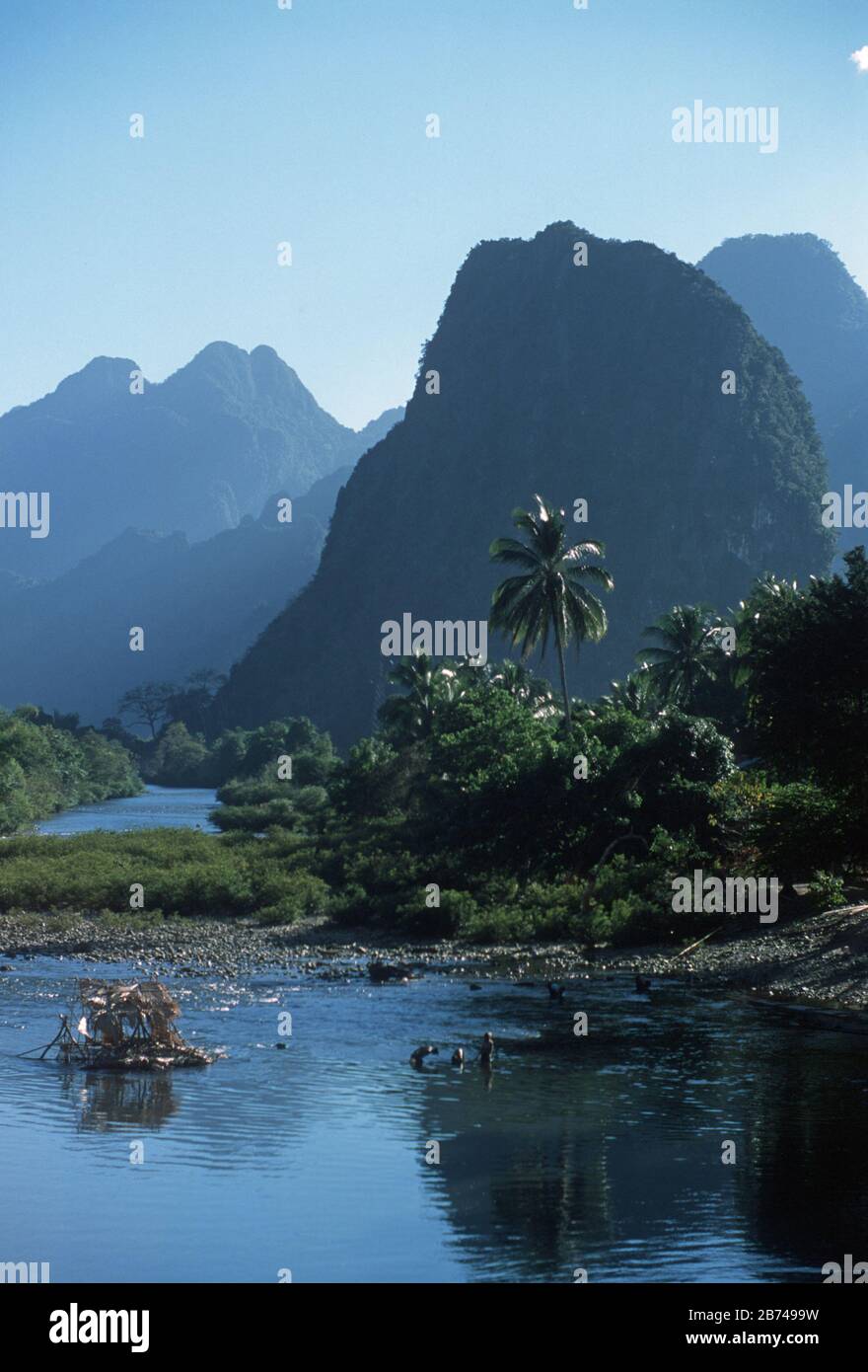 Tre uomini e una piattaforma di pesca nel fiume Nam Song a Vang Vien (Vang Vieng), nella provincia di Vientiane, Laos. Ci sono palme, alberi coperti, montagne carsiche e un cielo blu brillante dietro. Foto Stock