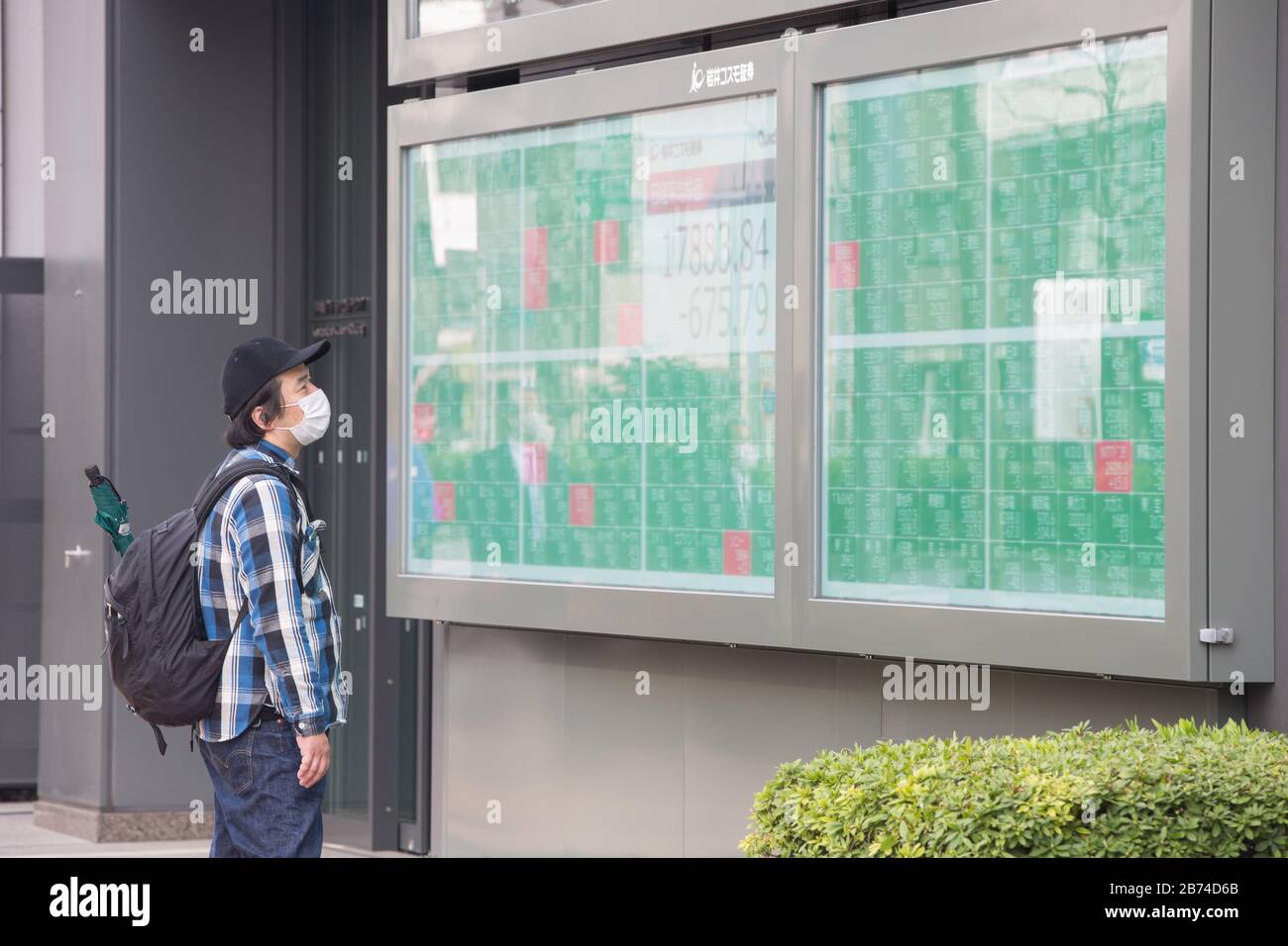 Un uomo con una maschera chirurgica come misura preventiva contro il virus corona, guarda una scheda elettronica che mostra i numeri per l'indice Nikkei 225 sulla Borsa di Tokyo a Tokyo. Foto Stock