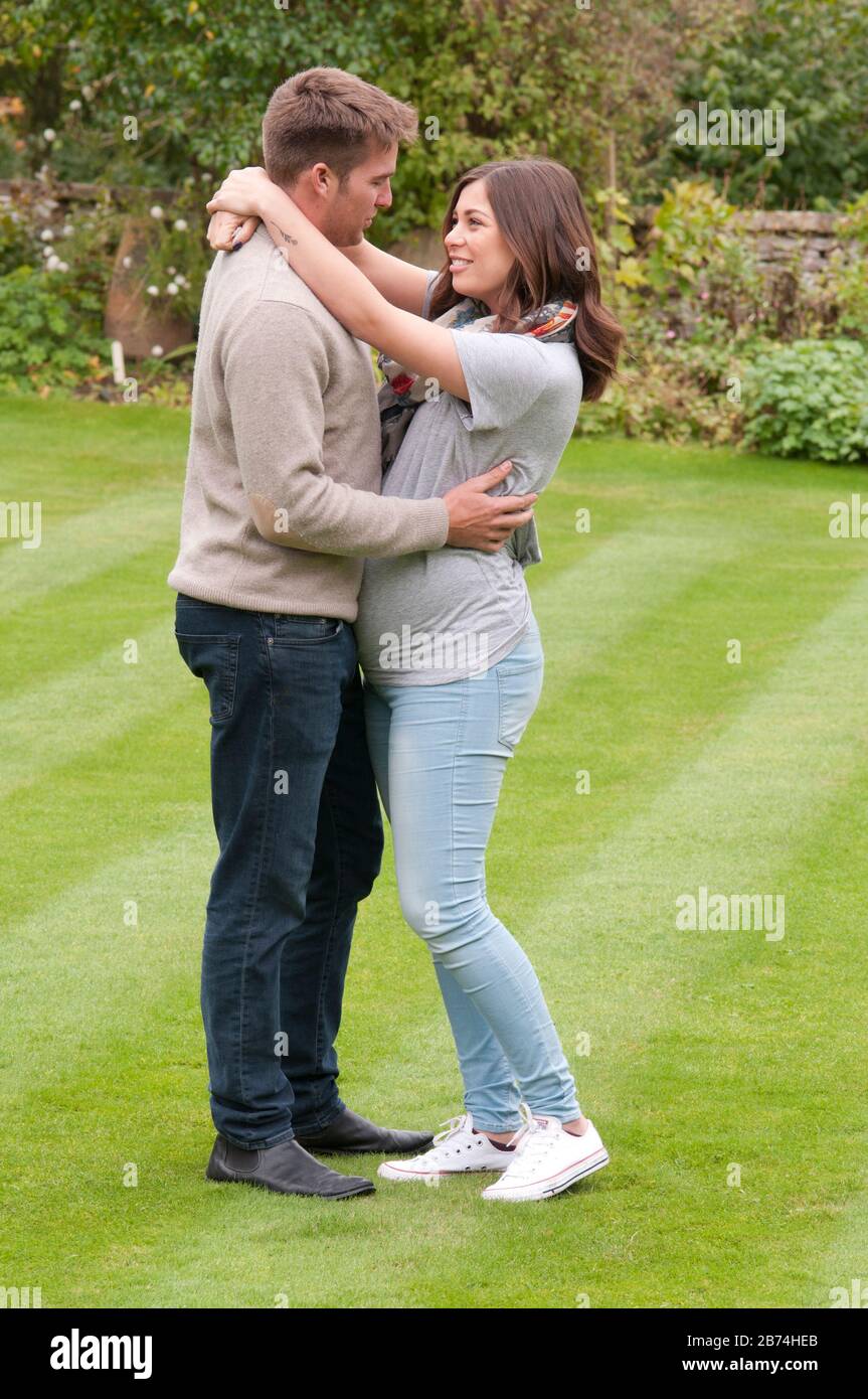 Bella giovane donna incinta e la sua partner con le braccia l'uno intorno all'altro Foto Stock
