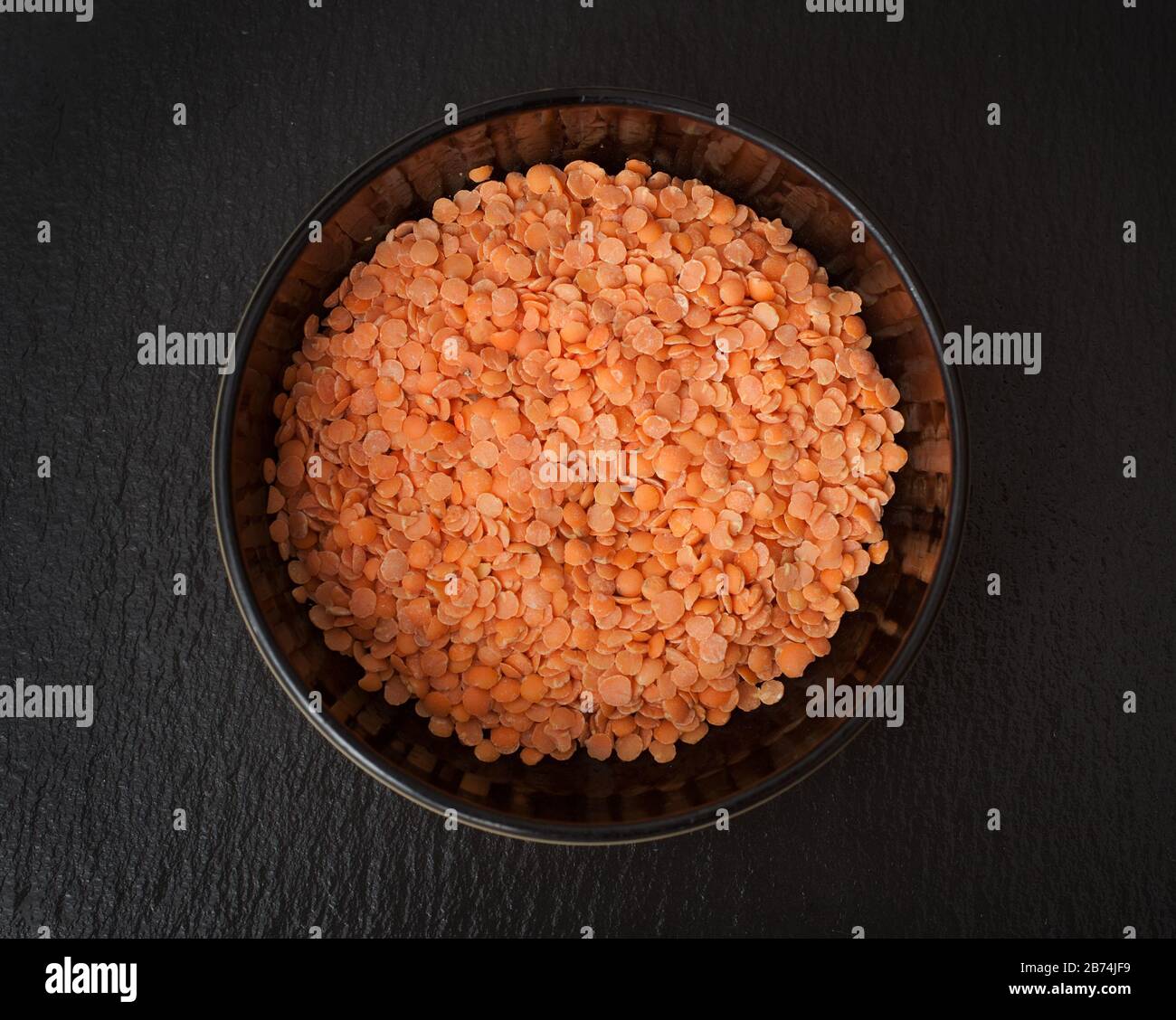 Una ciotola di lenticchie rosse crude su sfondo nero Foto Stock