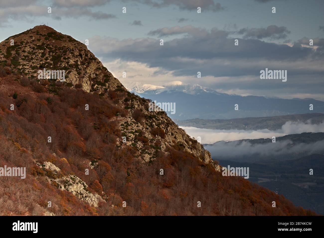 Montagna picco nella foresta autunnale, montagne innevate in lontananza e cielo nuvoloso, Montseny, Catalogna, Spagna Foto Stock