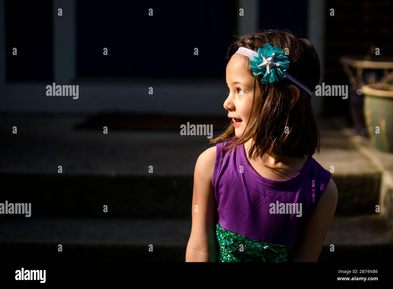 Una bella bambina in un archetto guarda sopra la sua spalla sorridente Foto Stock