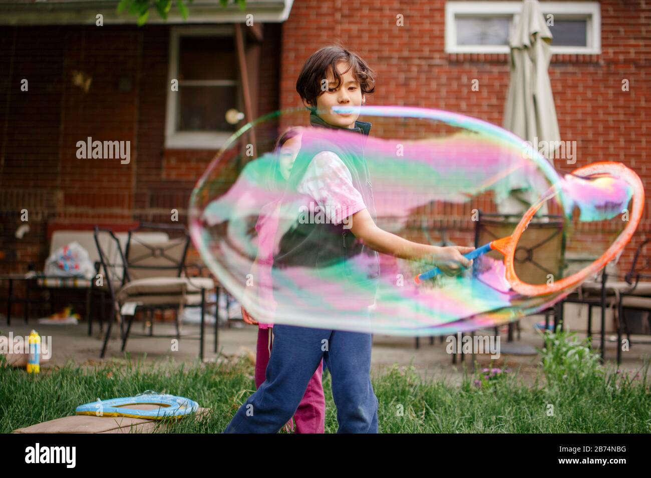Un ragazzo e sua sorella giocano con gigantesche bolle di sapone nel cortile posteriore Foto Stock