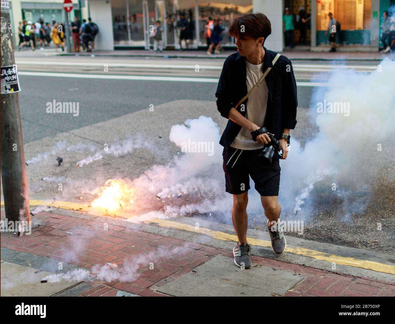 Un poliziotto lancia una granata gas lacrimogeni a un fotografo su una strada a Wanchai. La polizia disperde la folla durante un rally a Hong Kong. Foto Stock