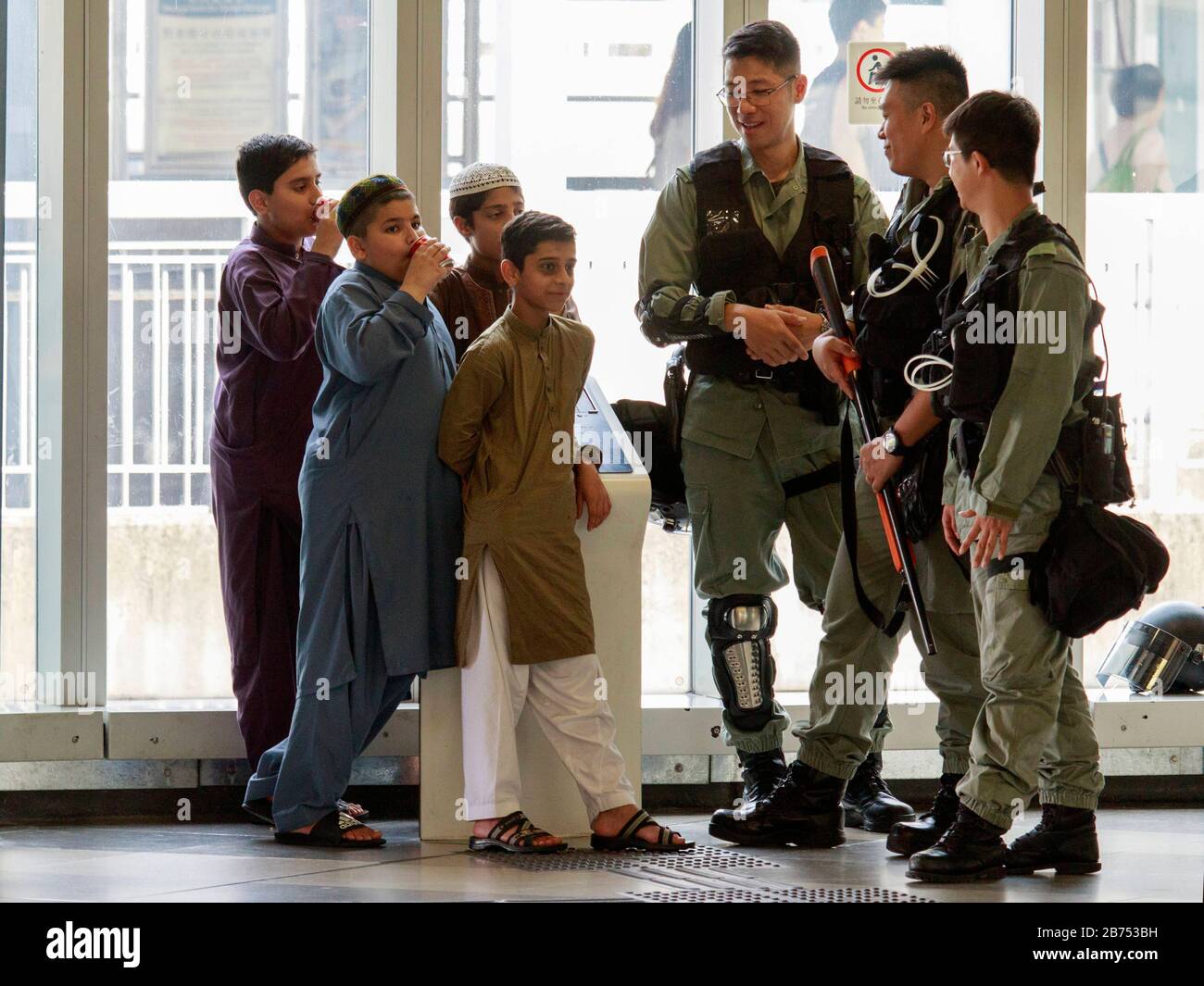 La polizia anti-riot chiacchiera con alcuni bambini sudasiatici in una stazione. Foto Stock