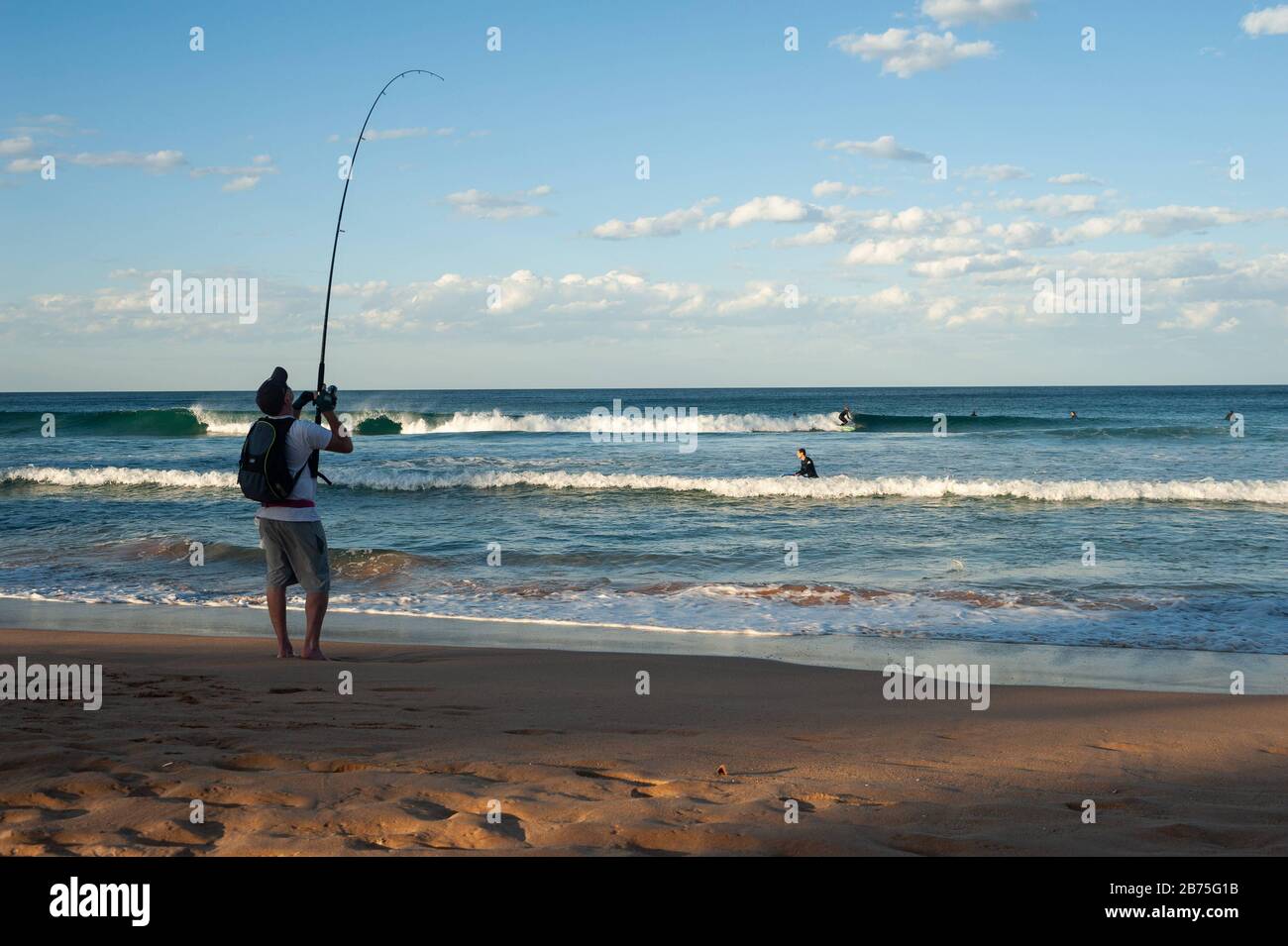 10.05.2018, Sydney, nuovo Galles del Sud, Australia - UN uomo è in piedi sulla spiaggia a Manly e la pesca, mentre in background surfisti sono in attesa per l'onda giusta. [traduzione automatica] Foto Stock