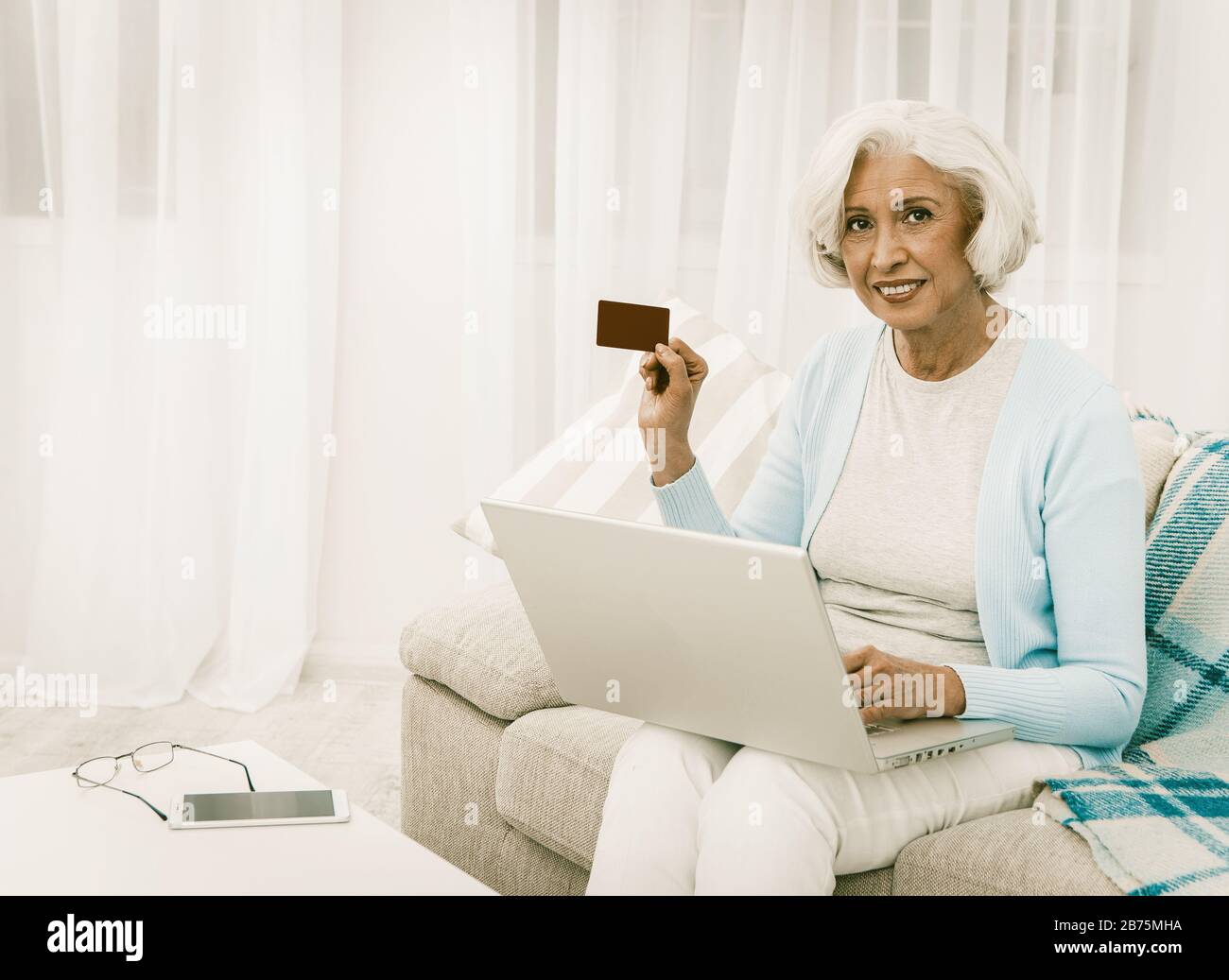 Donna anziana che usa il numero della carta di credito per l'acquisto delle merci nel mercato in linea Donna bella che usa il calcolatore del laptop e che mostra la carta di credito alla copia della macchina fotografica Foto Stock