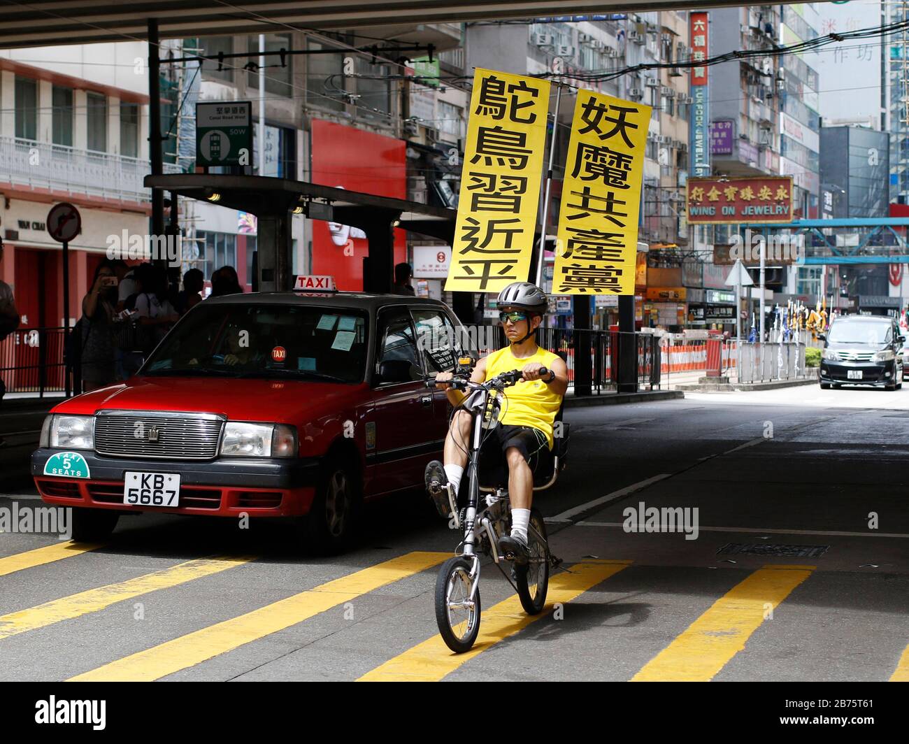 Un uomo pedola una bicicletta con una bandiera che recita:"Xi Jinping è uno struzzo, il partito comunista è demone' su una strada prima del raduno annuale pro-democrazia a Hong Kong, Cina, 01 luglio 2017. Il presidente cinese Xi Jinping ha inaugurato un nuovo Chief Executive di Hong Kong e ha celebrato il ventesimo anniversario della consegna della città dal governo britannico al dominio cinese il 01 luglio. Foto Stock