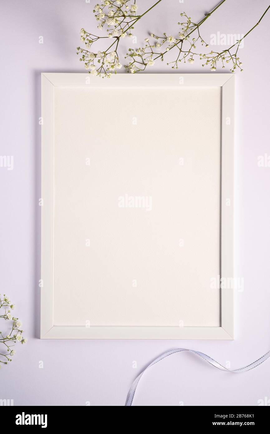Cornice bianca con dima vuota, fiori di gypsofila e nastro in tessuto, sfondo bianco, carta mockup Foto Stock
