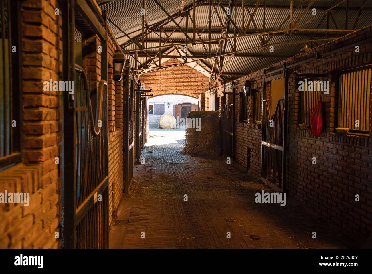 All'interno di una stalla di mattoni guardando attraverso una porta due rotoli di fieno e cavalli stalli Foto Stock