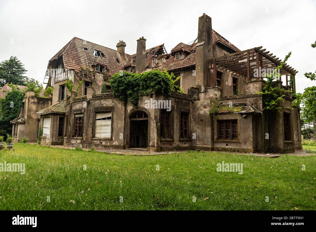 Vecchia casa abbandonata che ha preso fuoco con un giardino verde e un cielo nuvolato Foto Stock