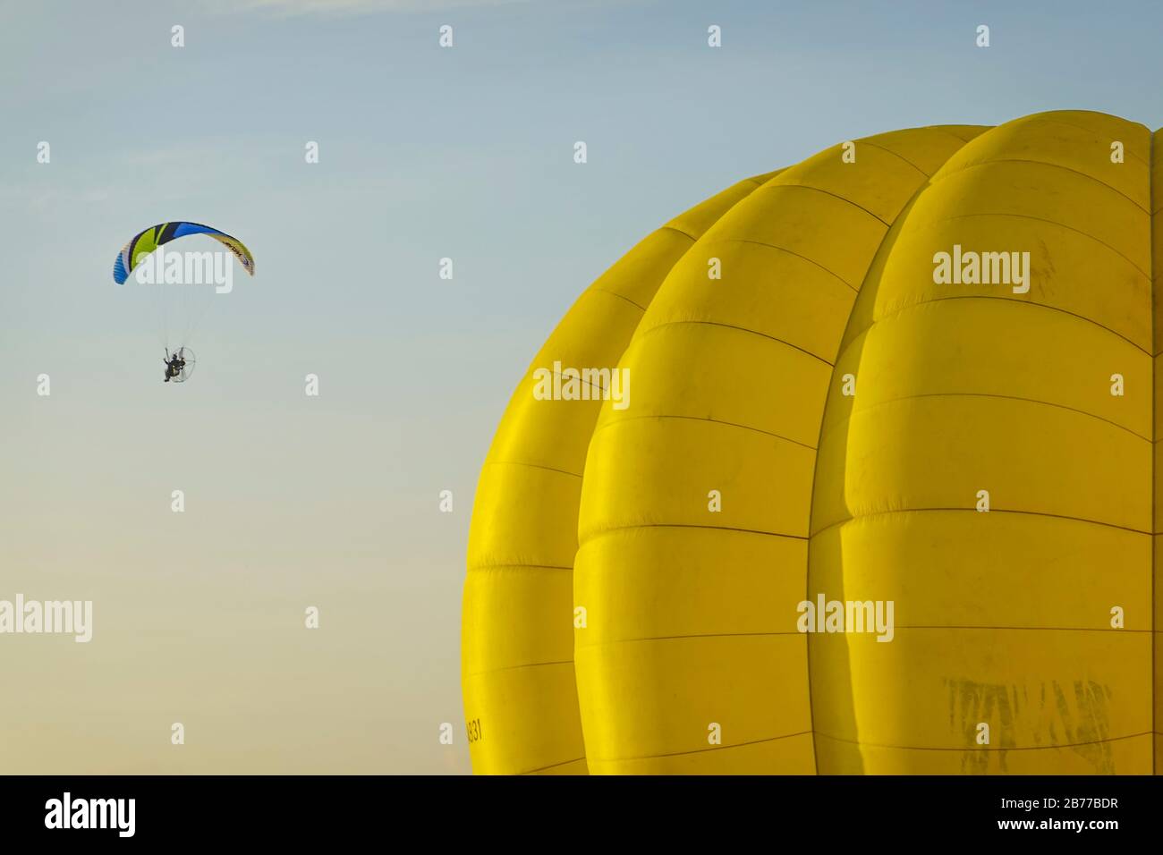 Un festival di mongolfiera presenta parapendio, mongolfiere e altri trasporti aerei. Un parapendio si aggira sopra un pallone prima che decolli. Foto Stock