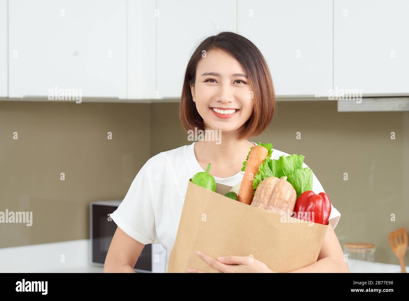 Felice, allegro donna asiatica holding sacchetto di carta pieno di prodotti freschi, ortaggi verdi, baguette e banane. Foto Stock