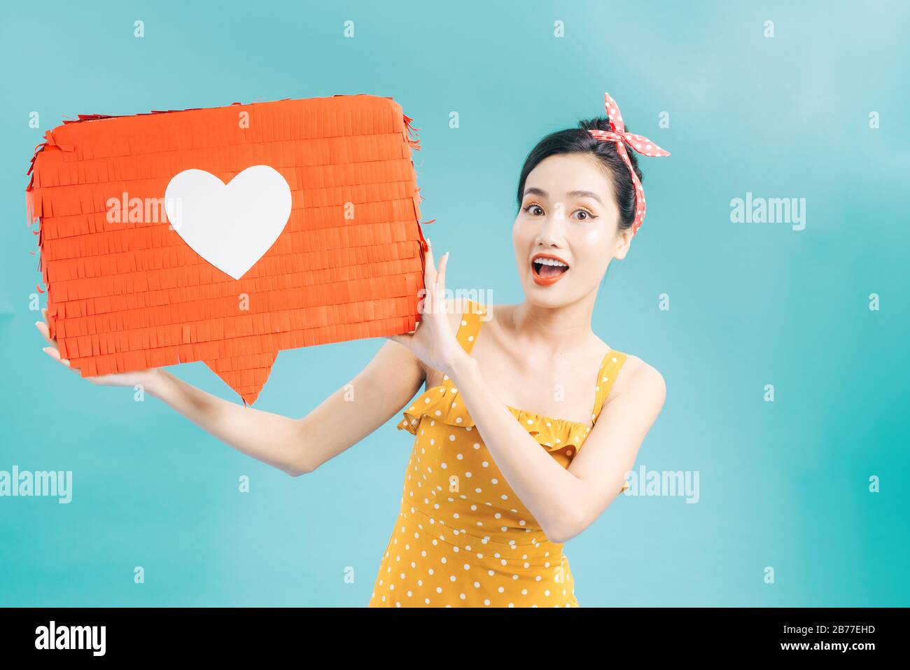 Ritratto di una allegra donna africana in piedi isolato su sfondo blu che mostra discorso bolla con icona a forma di cuore Foto Stock