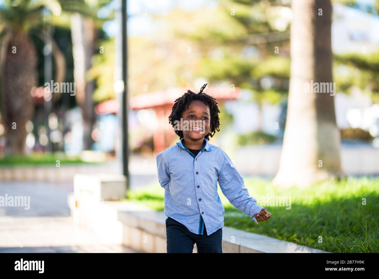 Felice e bella giovane ragazzo nero razza africana con etnico alternativo capelli giocare e rinnig in un parco giochi con e divertirsi - strada in città Foto Stock